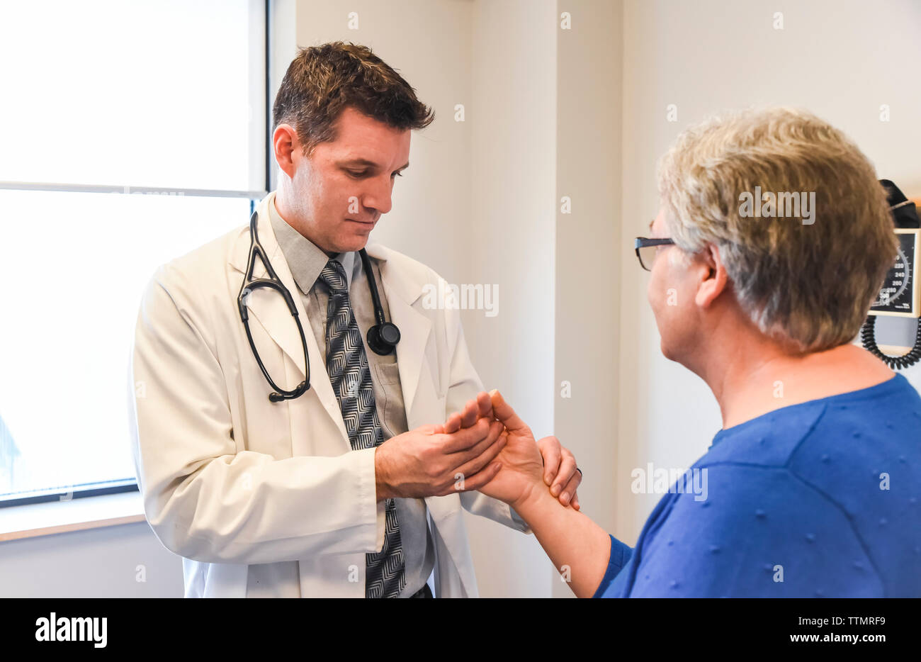 Doctor taking pulse of older female patient in clinical setting. Stock Photo