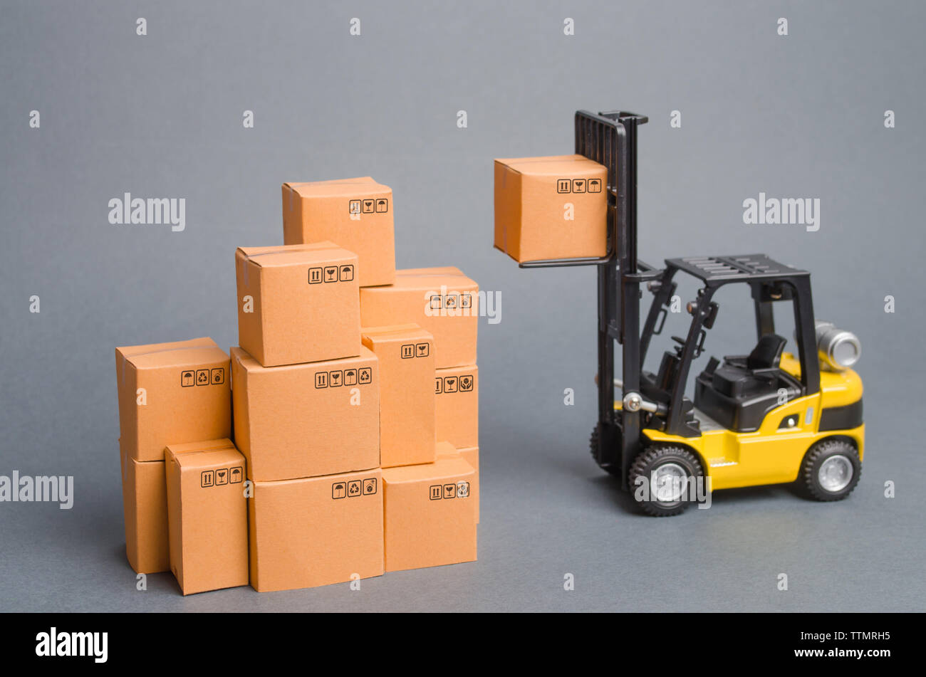 Yellow Forklift truck raises a cardboard box to the top of a stack pile ...