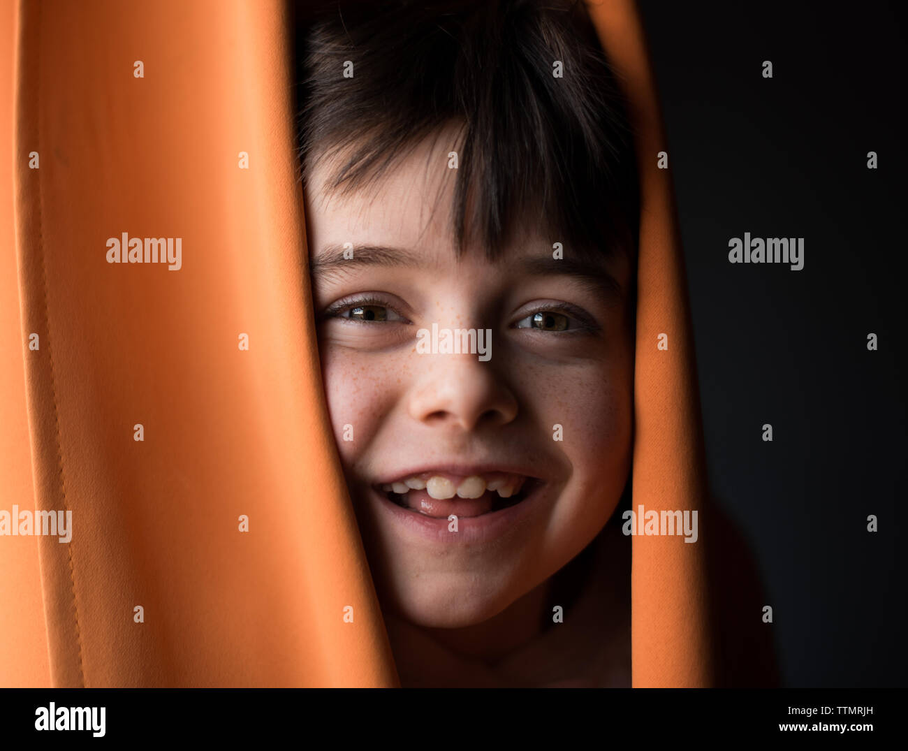 Portrait of a young happy boy peeking his head through curtains. Stock Photo