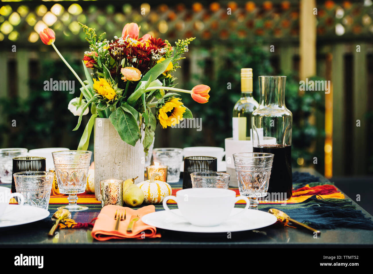 Flower vase with place setting and wine bottles on dining table in backyard Stock Photo