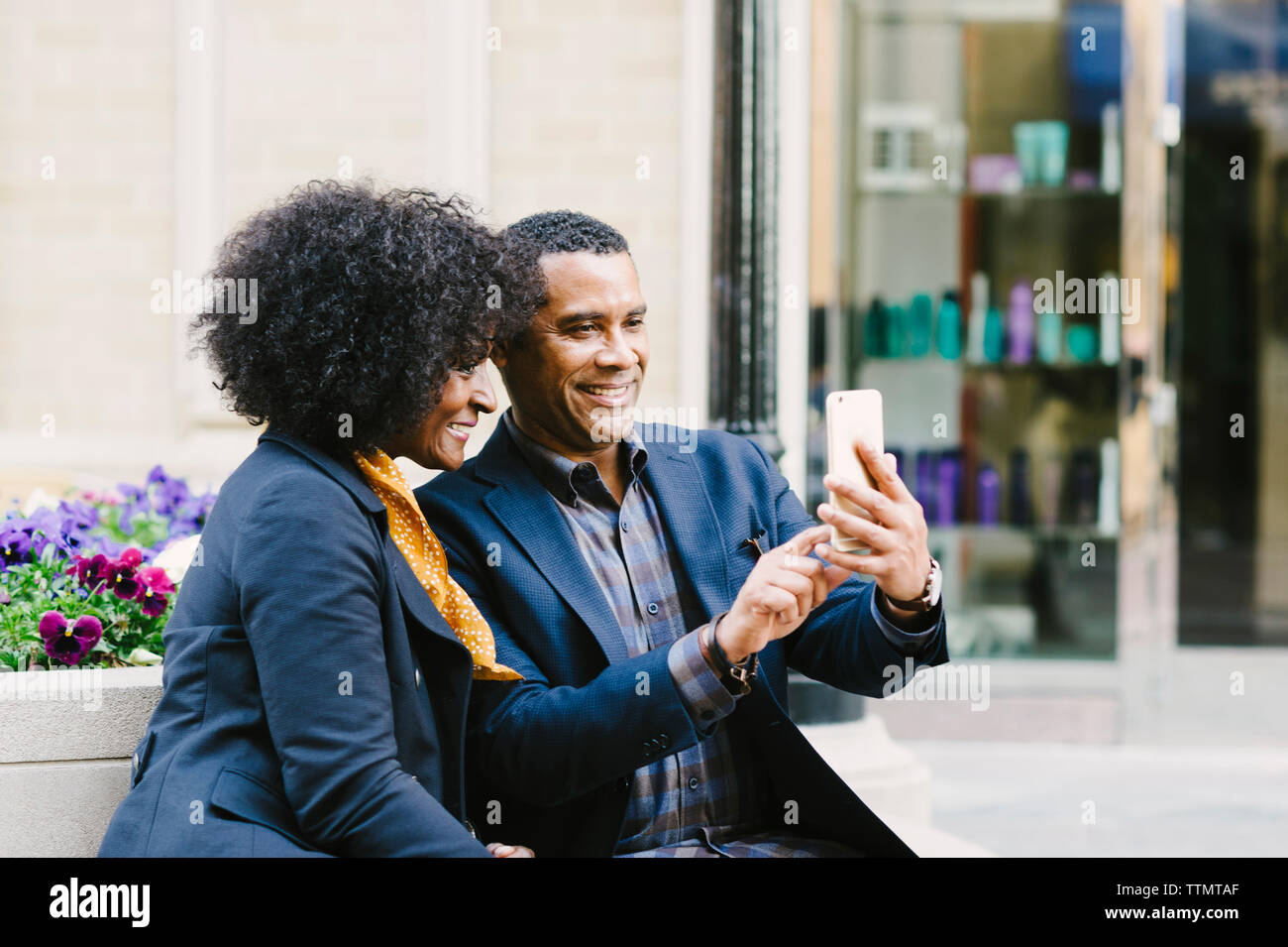 Happy couple taking selfie through mobile phone while sitting on seat in city Stock Photo