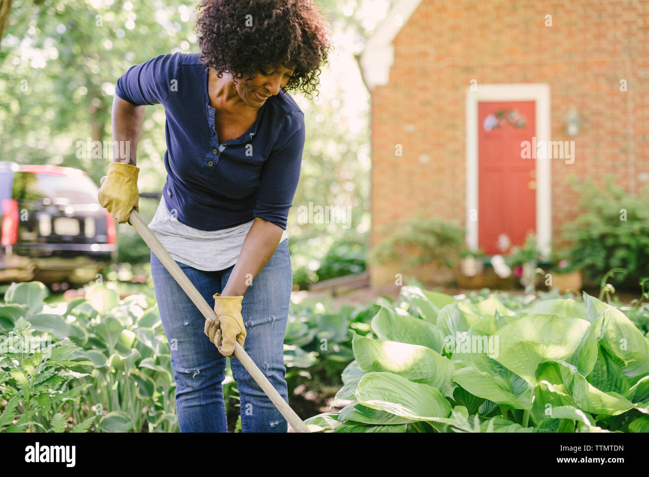 Mature woman using gardening fork while working in yard Stock Photo