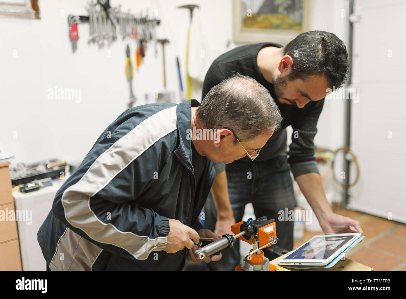 Mechanics watching tablet computer while operating equipment at workshop Stock Photo