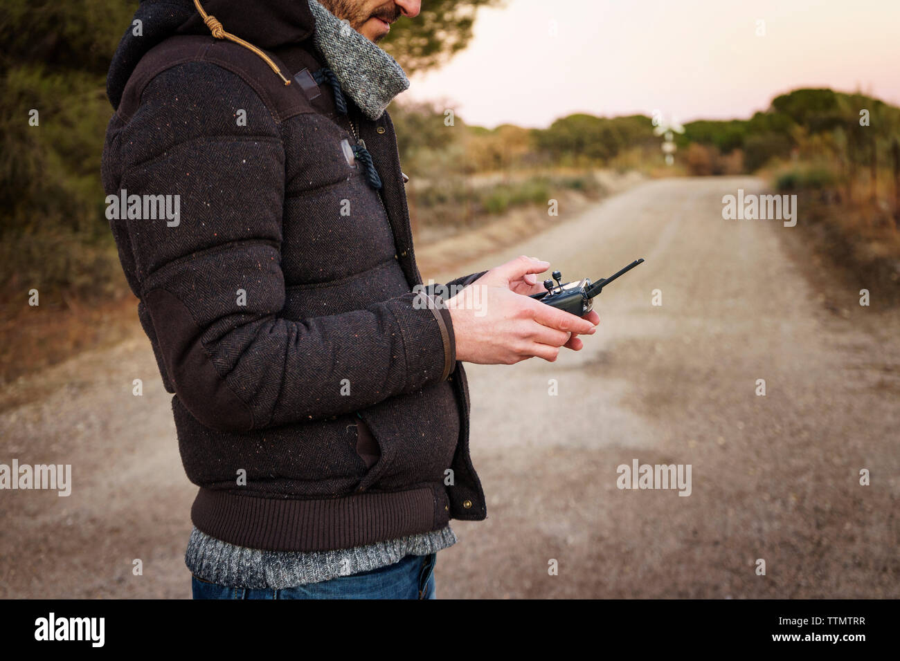 Midsection of man operating drone's remote control while standing on dirt road Stock Photo