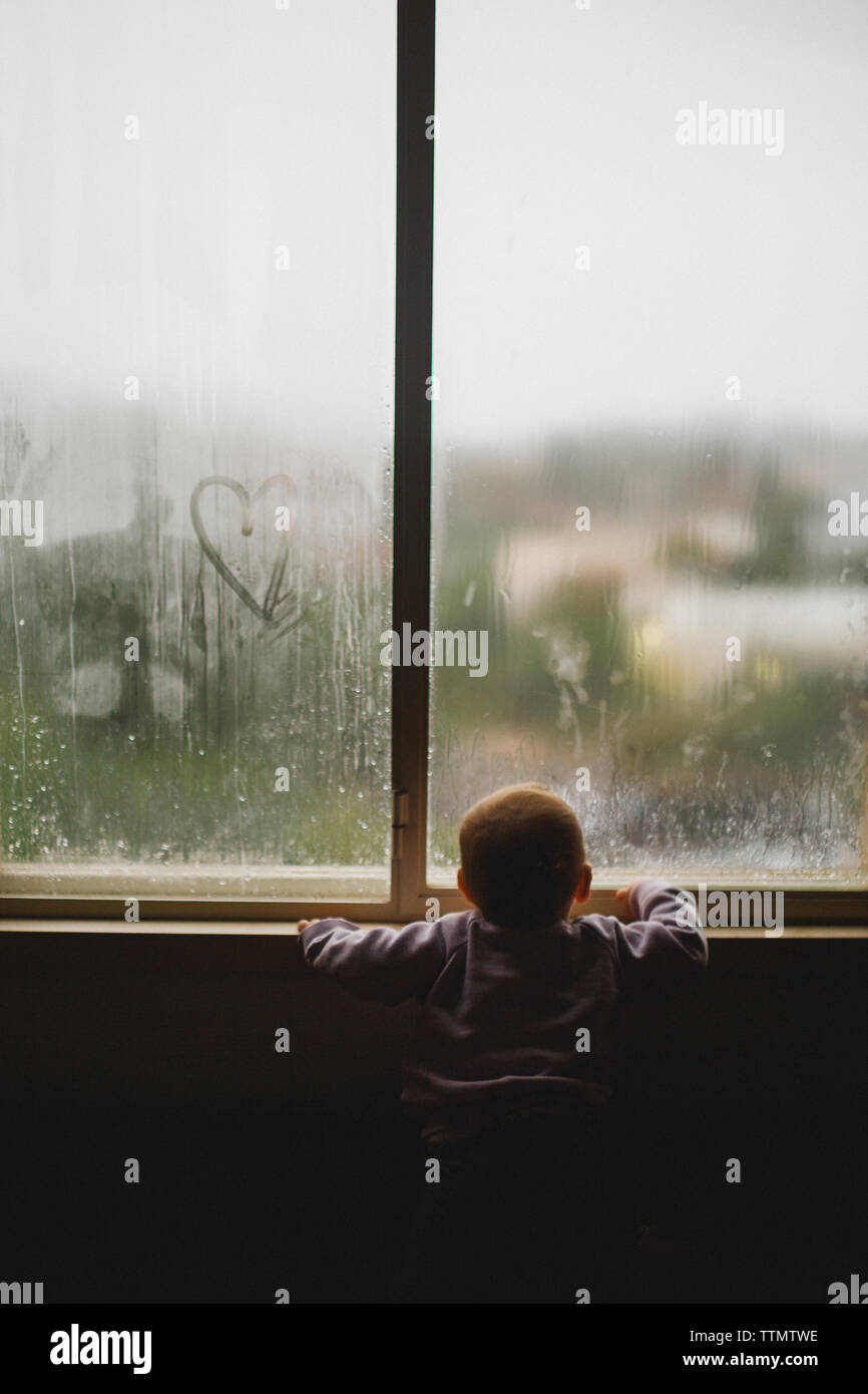 A baby girl looking through a window covered with steam and heart Stock Photo