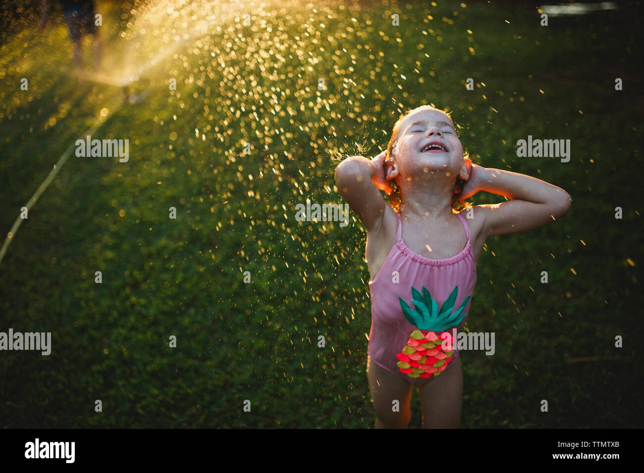 A young girl wearing bathing suit playing on the grass with sprinkler Stock Photo