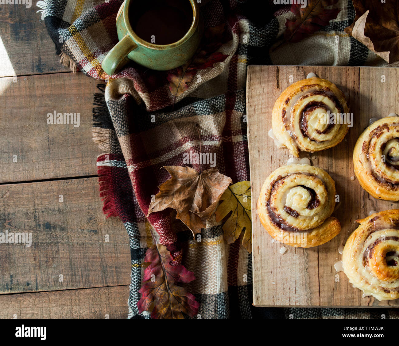 Overhead view of cinnamon rolls by autumn leaves with coffee and blanket on wooden table Stock Photo