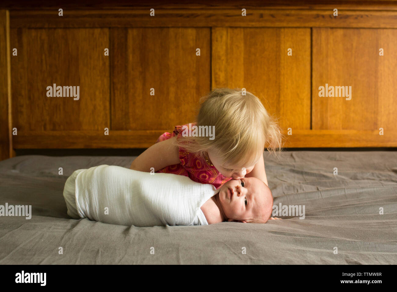 Girl kissing brother lying on bed at home Stock Photo