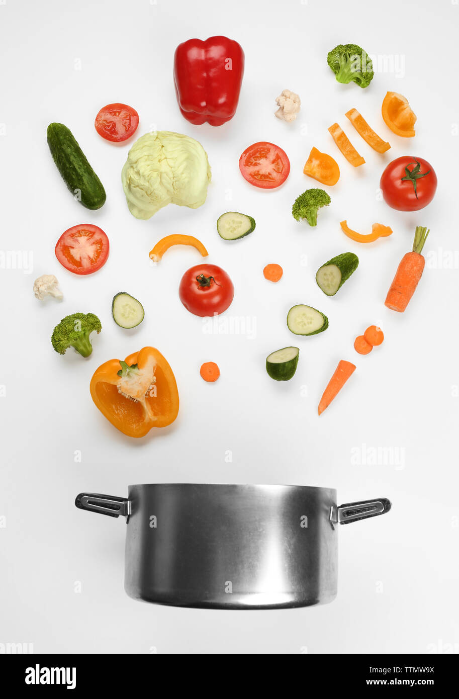 Fresh vegetables falling into a casserole pot on white background Stock Photo