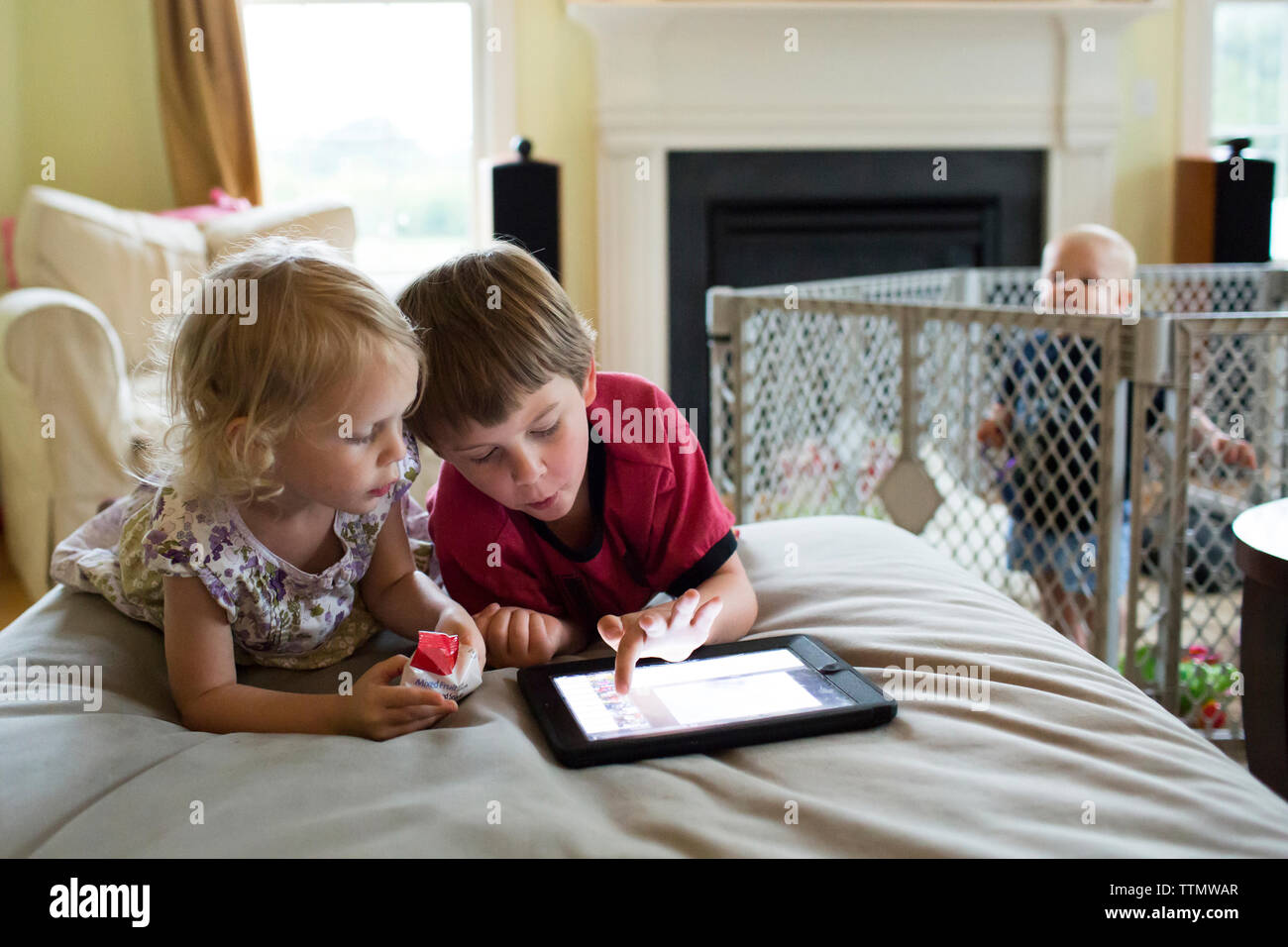 Baby boy looking at siblings using tablet computer while standing in crib Stock Photo