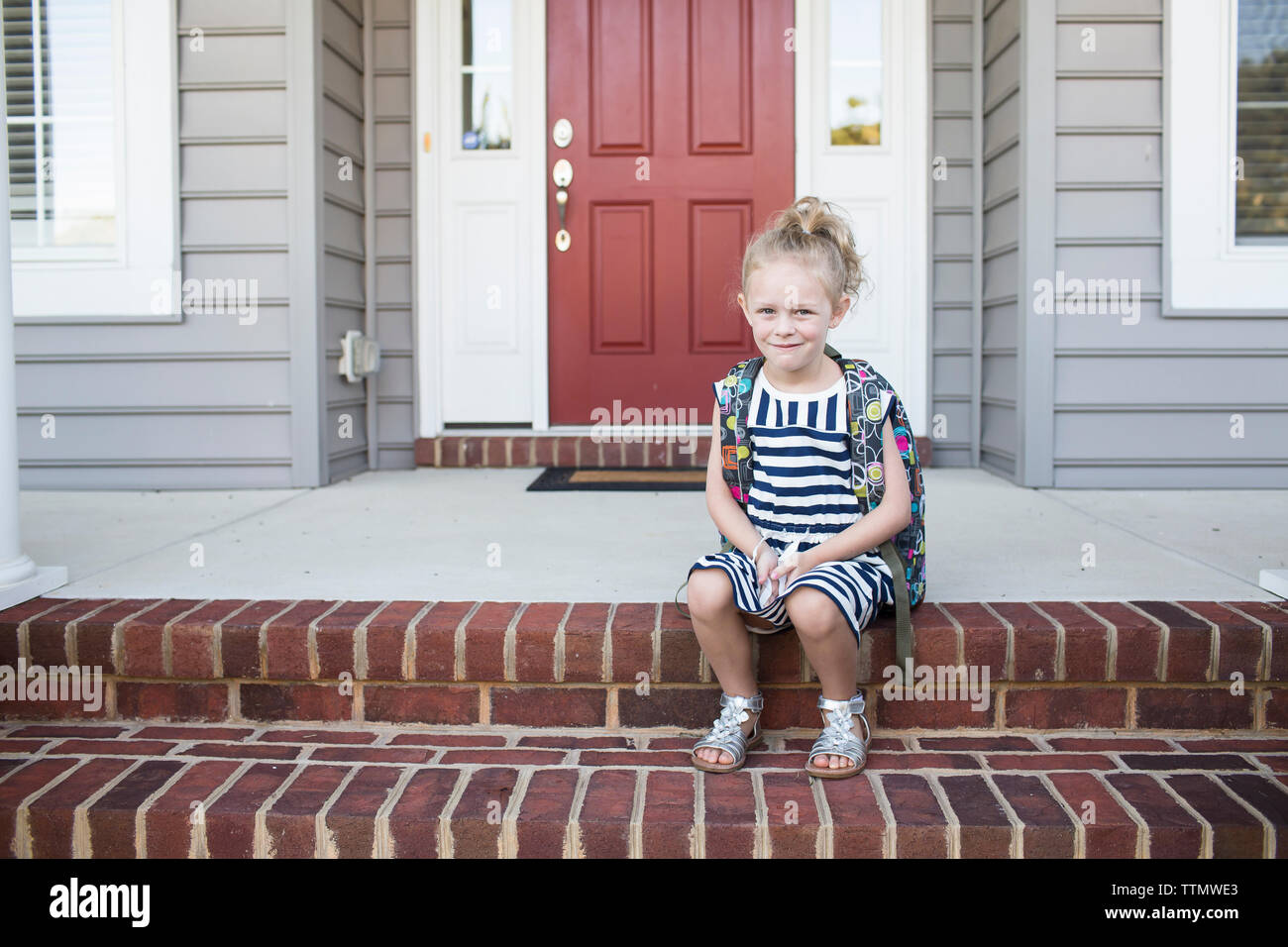 Portrait of schoolgirl sitting on steps in front of house Stock Photo
