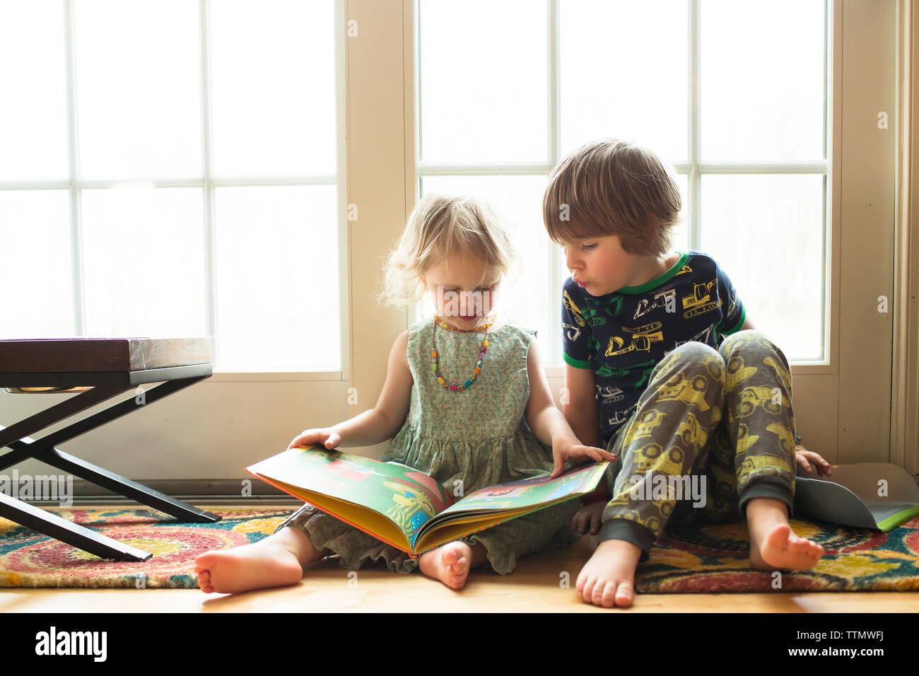 Siblings looking at picture book while sitting by window at home Stock Photo
