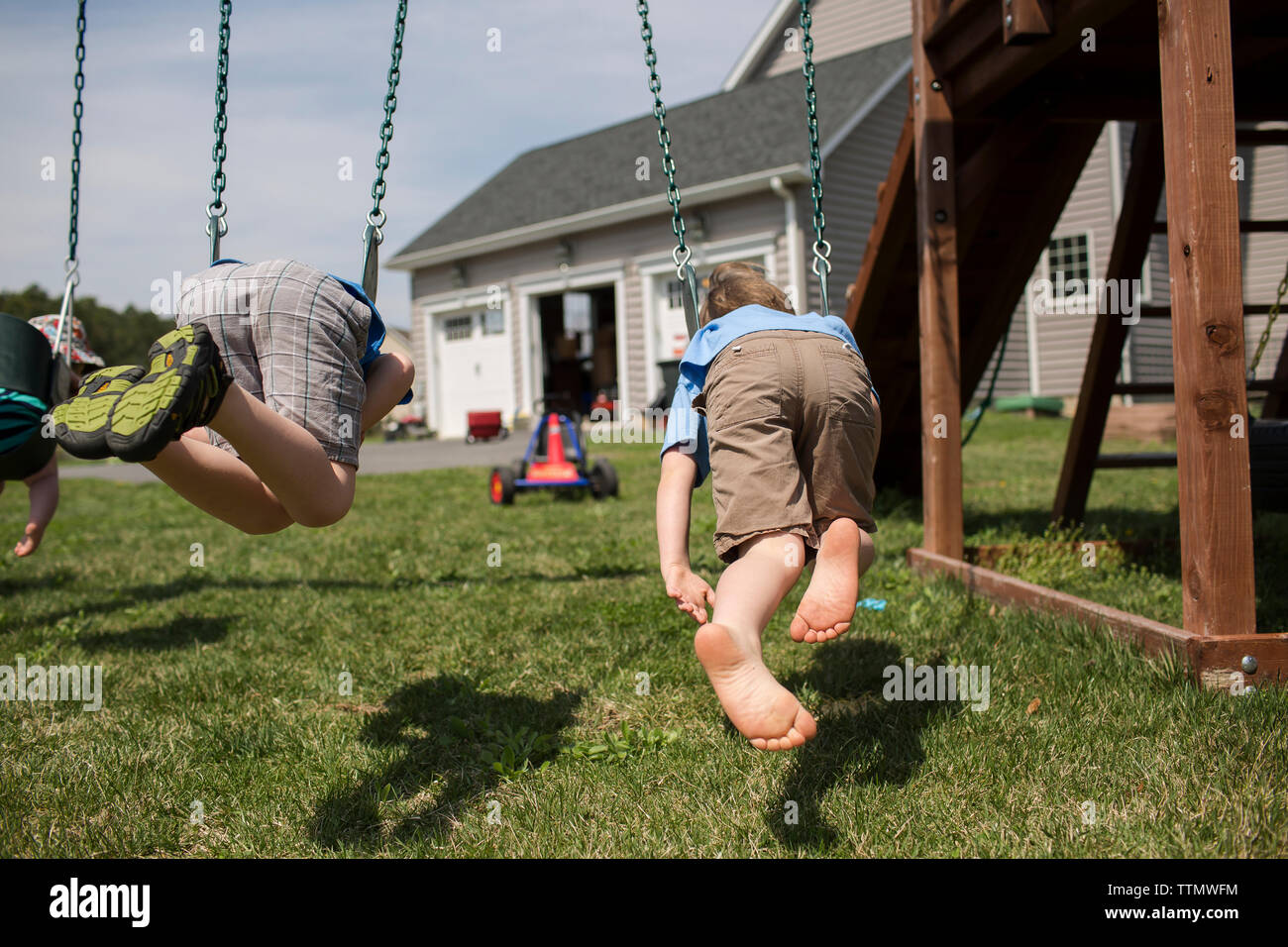 Brothers swinging in backyard during sunny day Stock Photo