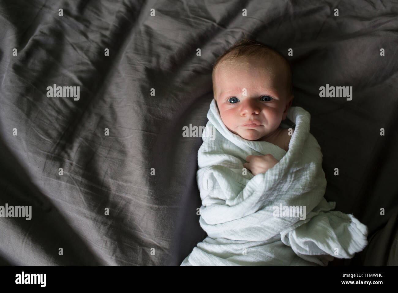 Overhead portrait of baby boy lying on bed while being wrapped in
