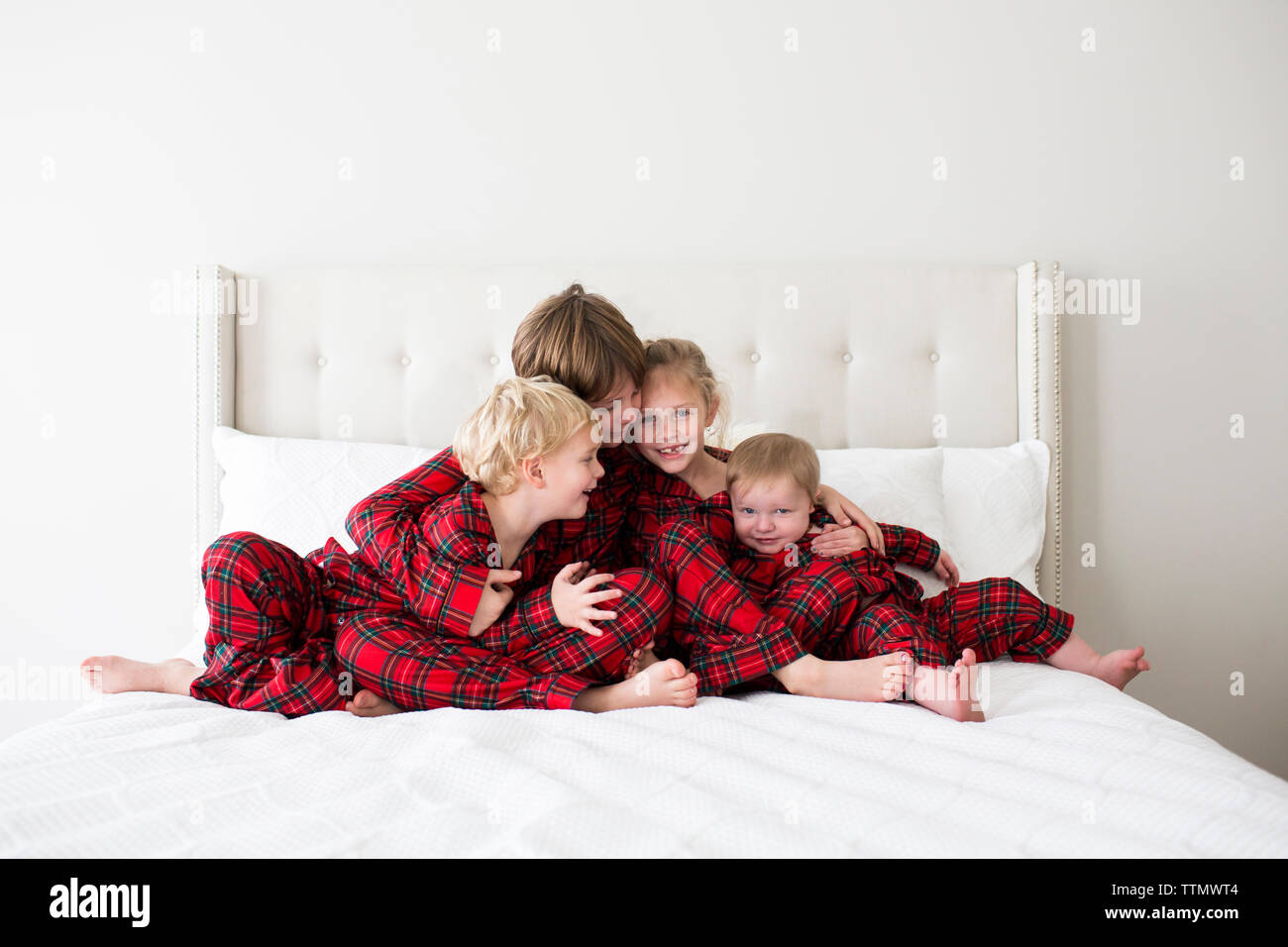 Four Toddler to Tween Siblings in Tartan Pajamas Hugging on White Bed Stock Photo