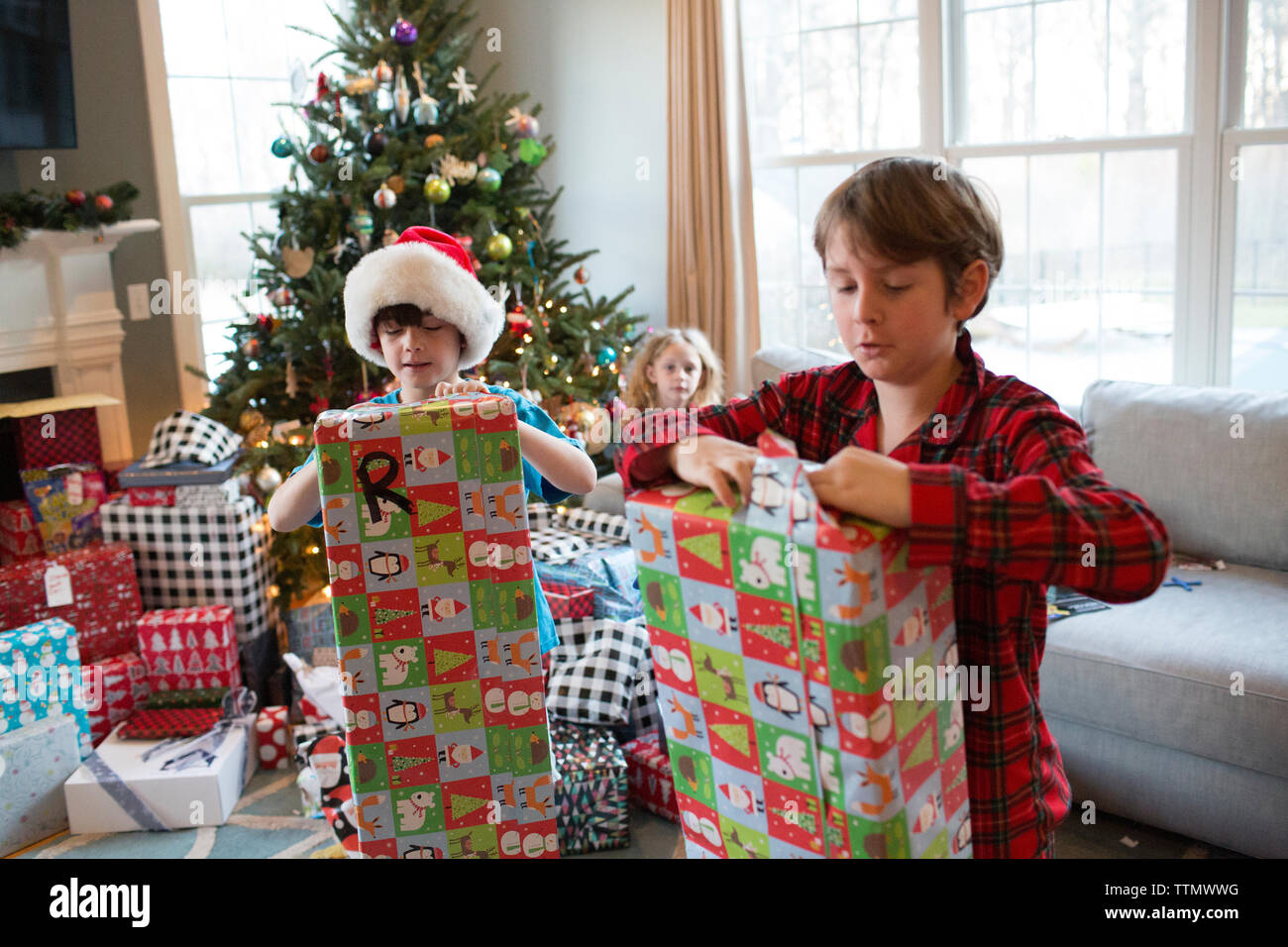 Cousins Opening Colorful Christmas Gifts While Little Sister Watches Stock Photo