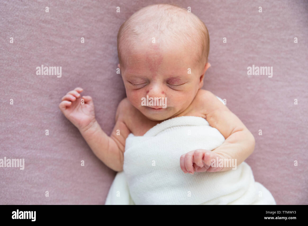 Close up Newborn Baby Girl in White Wrap Laying on Pink Blanket Stock Photo