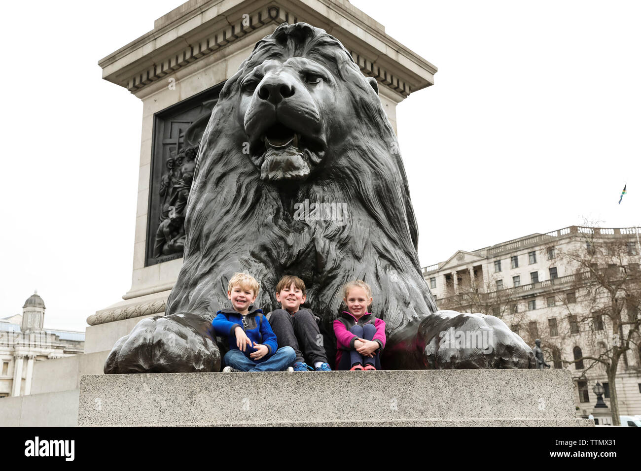 Three Smiling Siblings Sit on the Trafalgar Square Lion Stock Photo