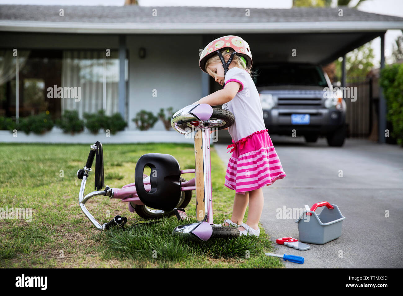 Side view of girl repairing bicycle on footpath outside house Stock Photo