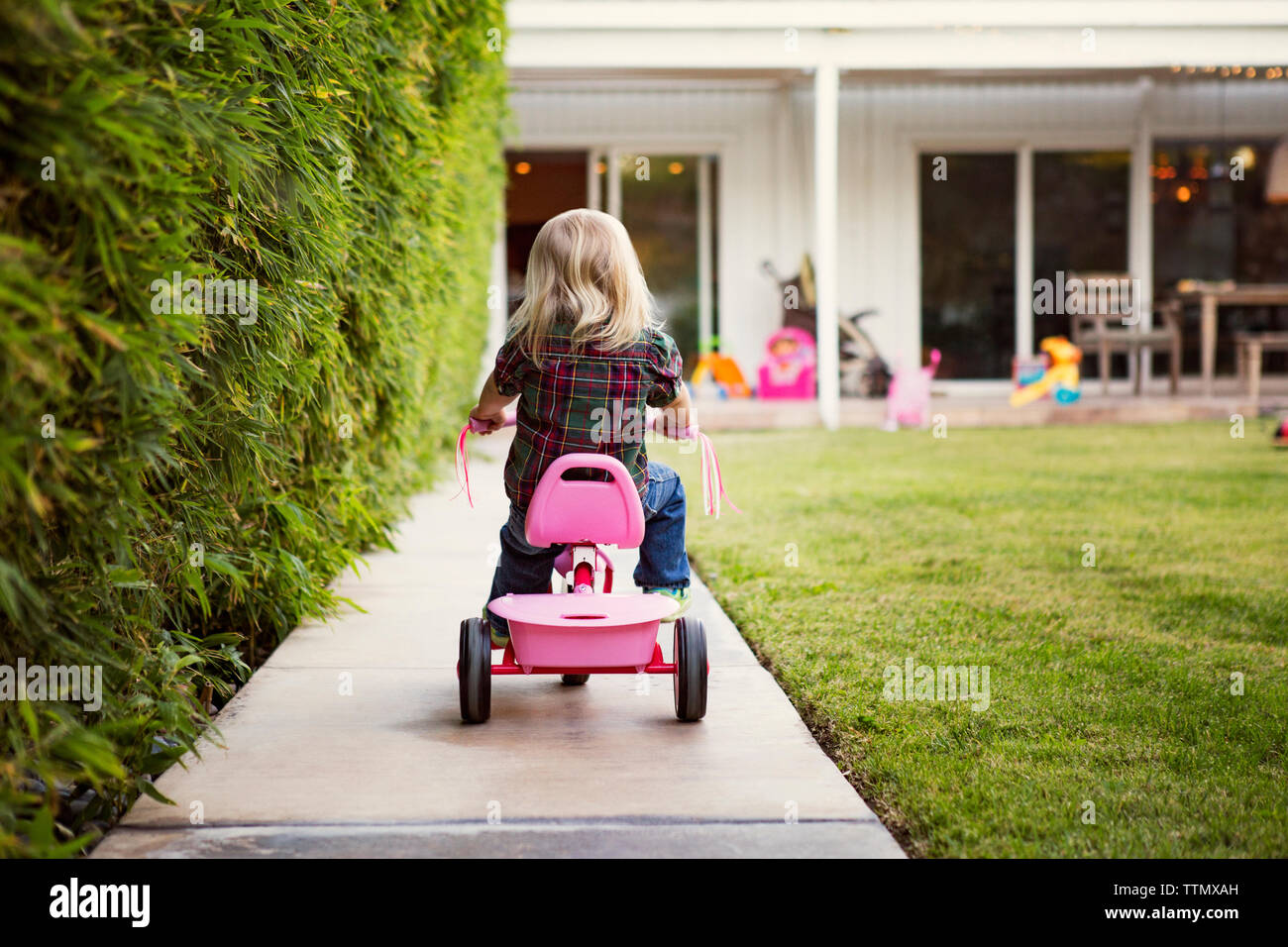 Rear view of girl riding tricycle at yard Stock Photo