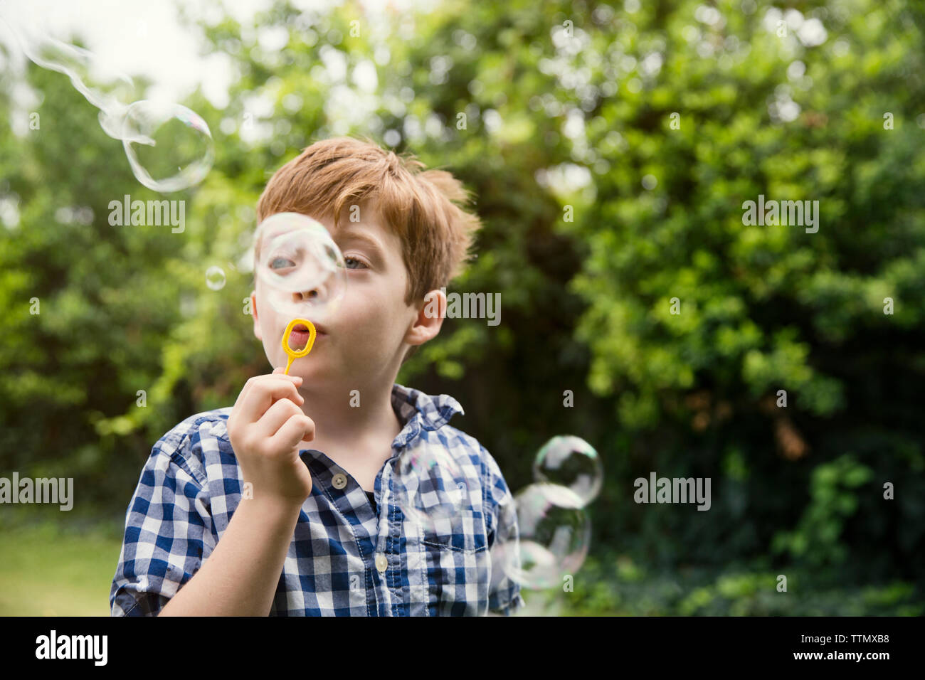 Thoughtful boy blowing bubbles in yard Stock Photo