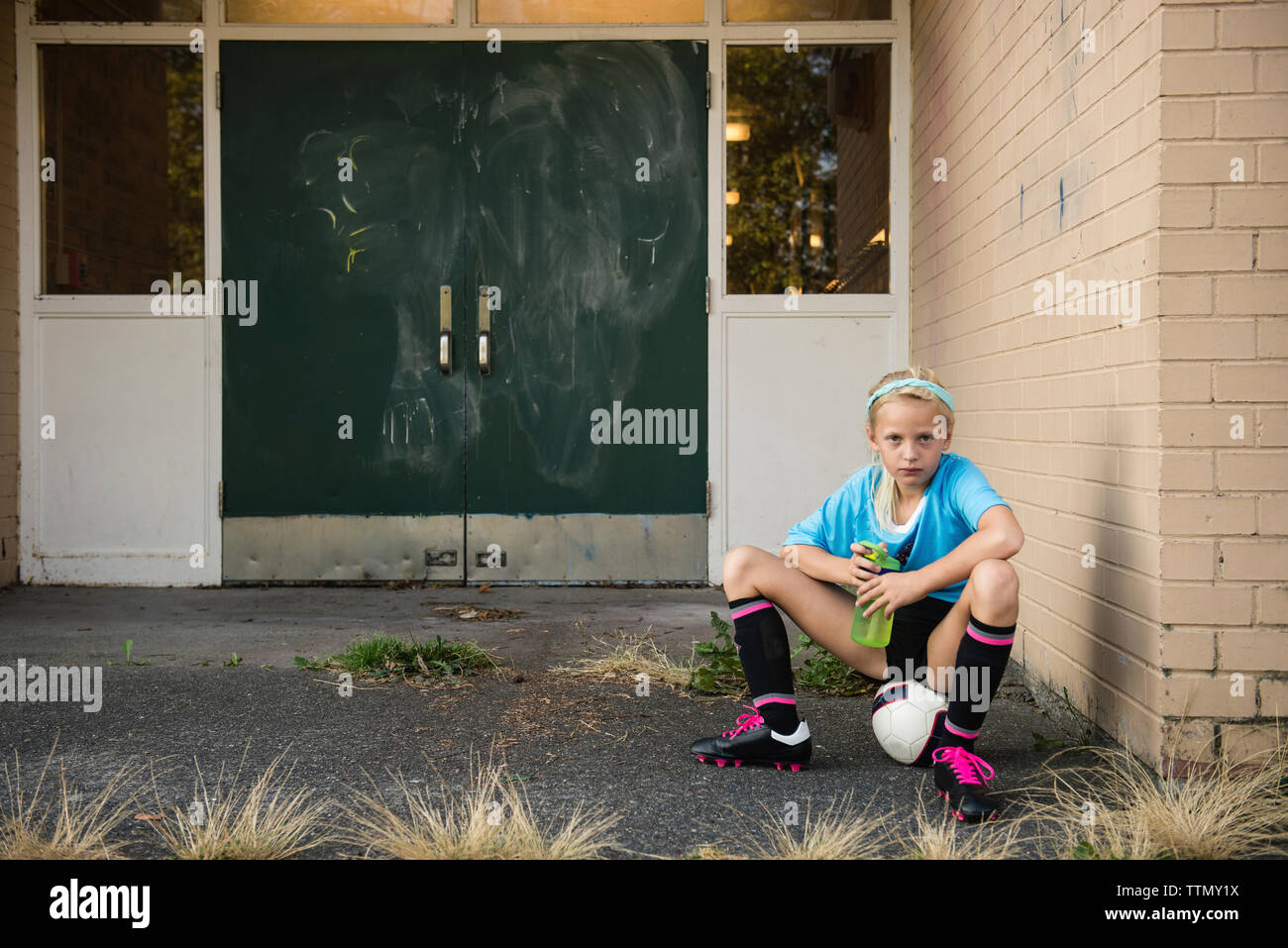 Portrait of girl in sports uniform holding water bottle while sitting on ball at yard Stock Photo