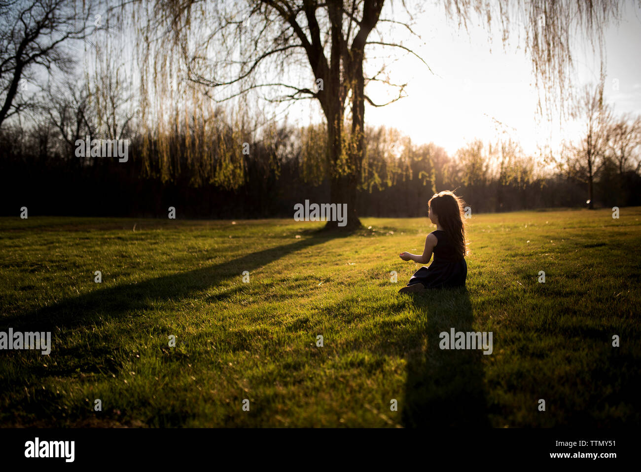Girl sitting on grassy field during sunset Stock Photo - Alamy