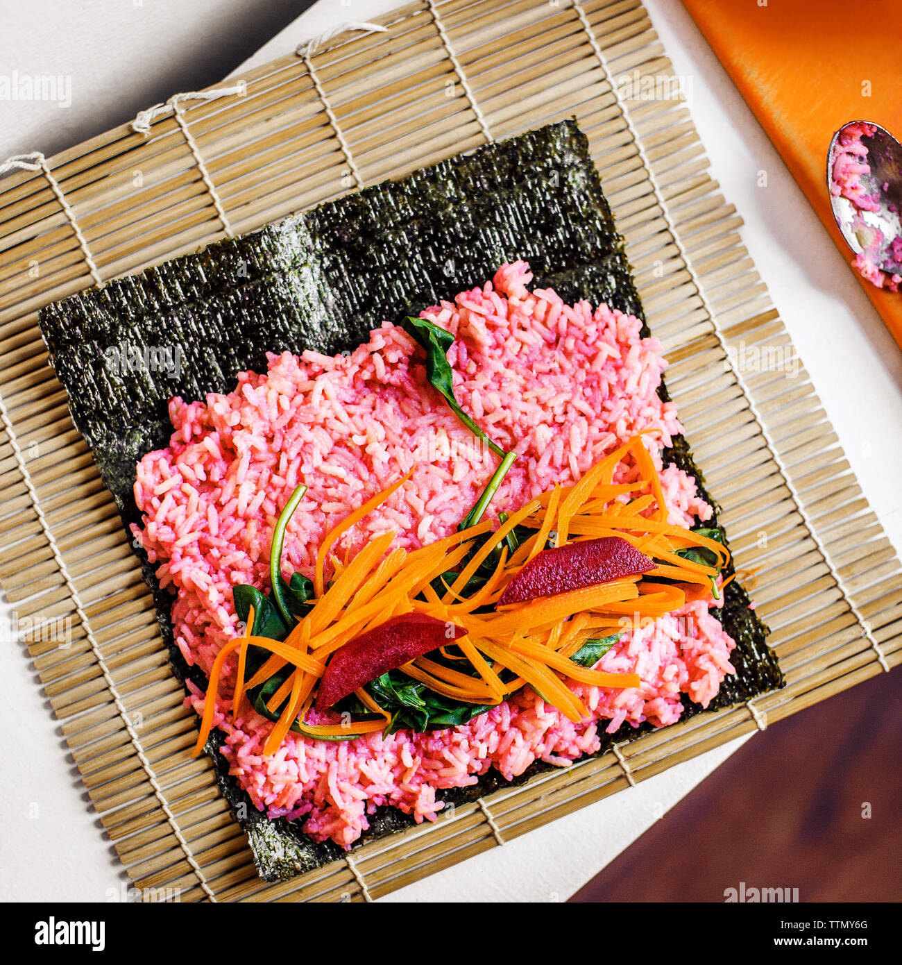 Overhead view of vegetables and sushi rice on nori at table Stock Photo