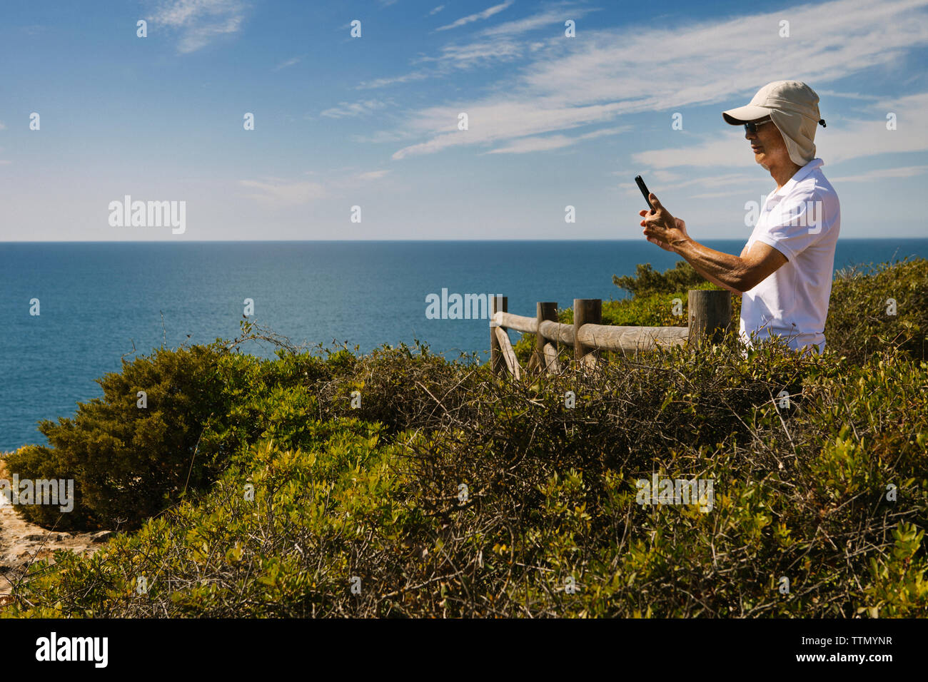 Man using phone while standing on cliff by sea against sky Stock Photo