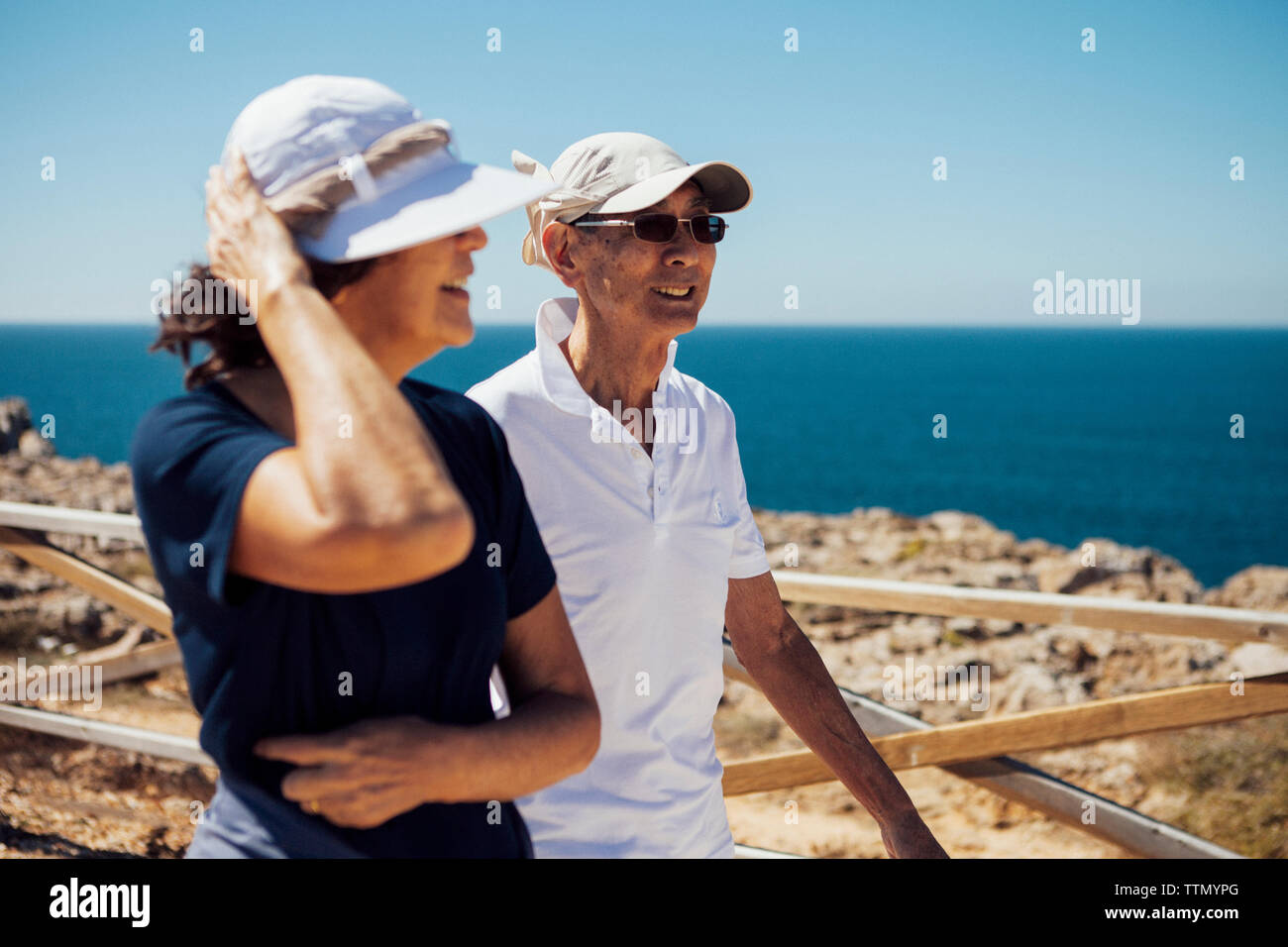 Smiling senior couple looking at sea while standing by railing against clear sky Stock Photo