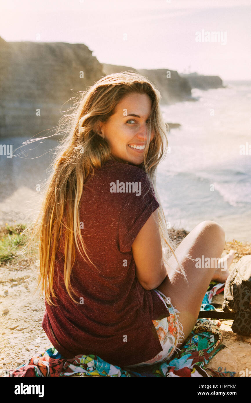 Portrait of happy woman sitting on cliff by sea against sky Stock Photo