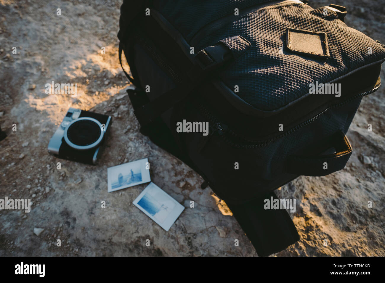 High angle view of camera with instant photographs and luggage on rock formation during sunset Stock Photo