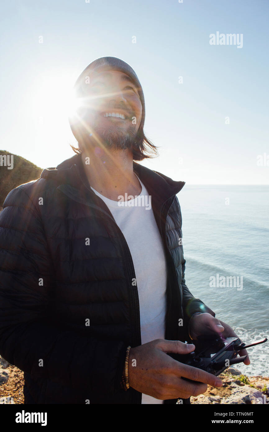 Smiling man holding remote control while standing at beach against clear sky during sunny day Stock Photo