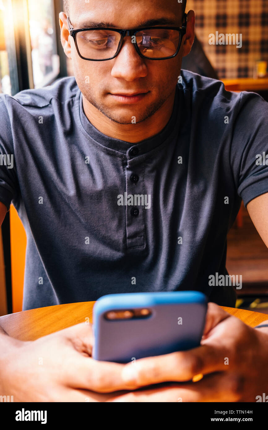 Young man wearing eyeglasses using mobile phone in cafe Stock Photo