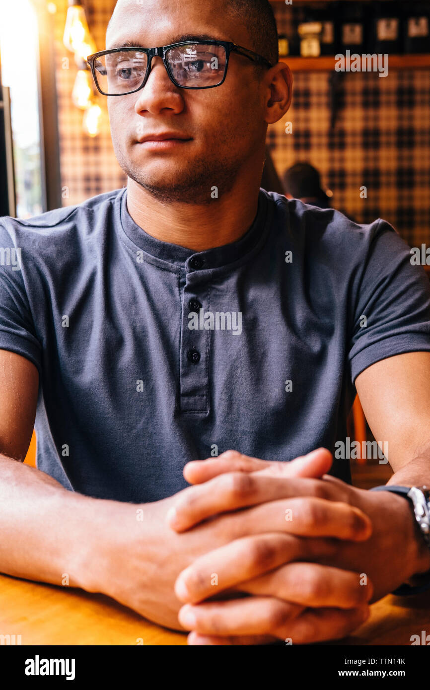Thoughtful young man with hands clasped looking away in cafe Stock Photo