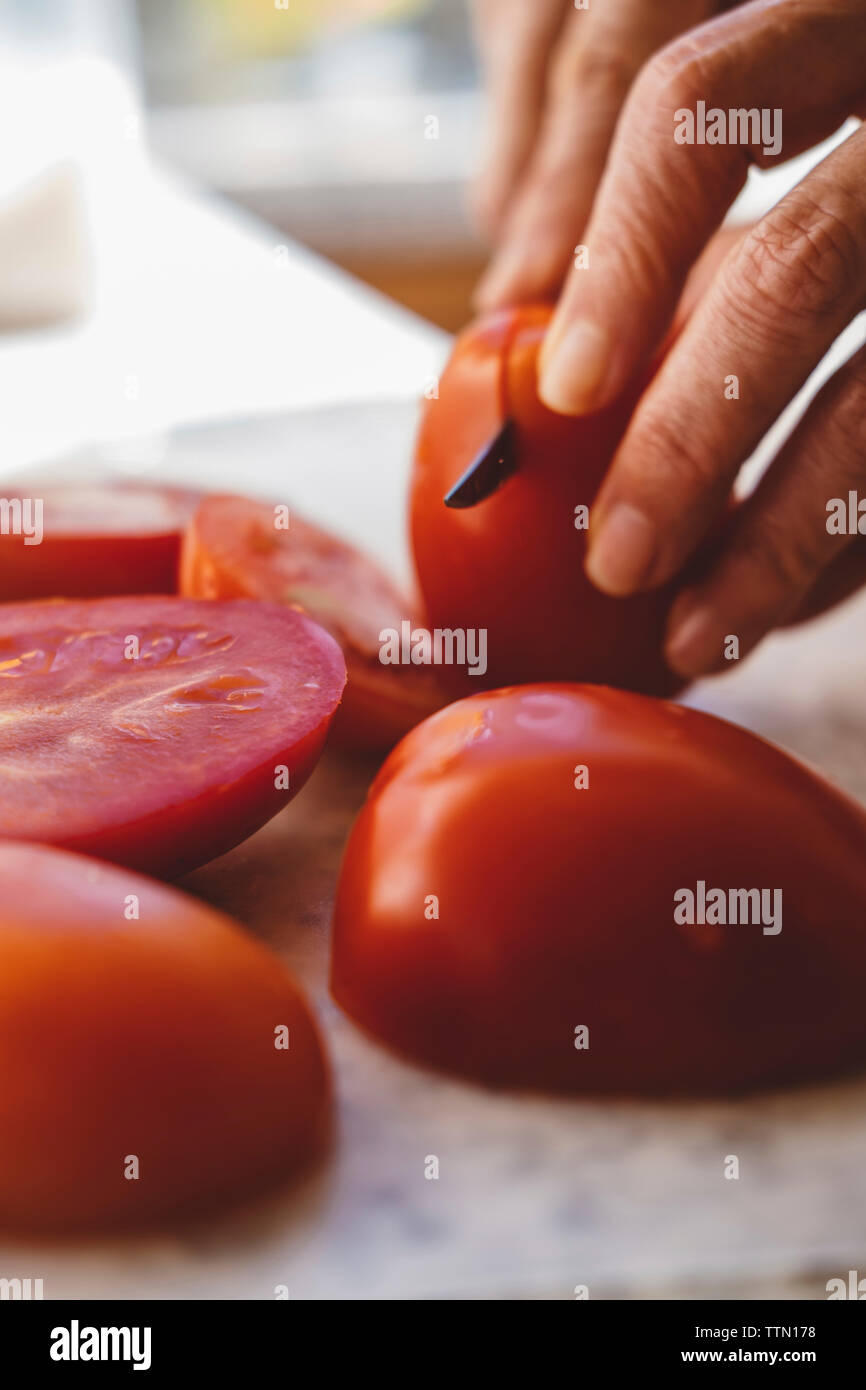Cropped hands of woman cutting tomatoes on table in kitchen Stock Photo