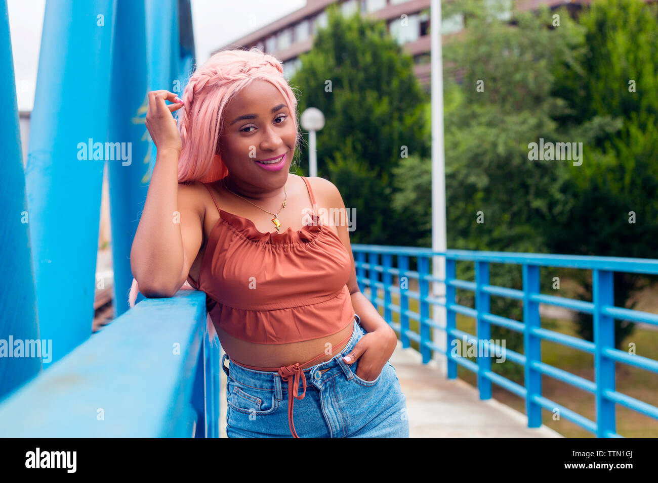 Portrait of smiling woman with pink hair standing by railing on footbridge Stock Photo