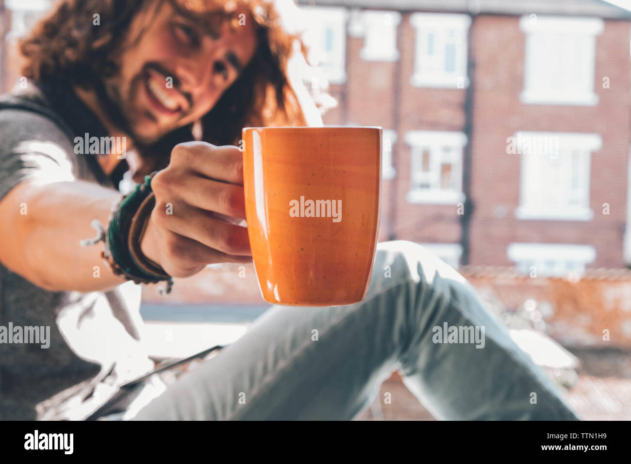Caucasian offering his coffee mug while smiling at camera Stock Photo