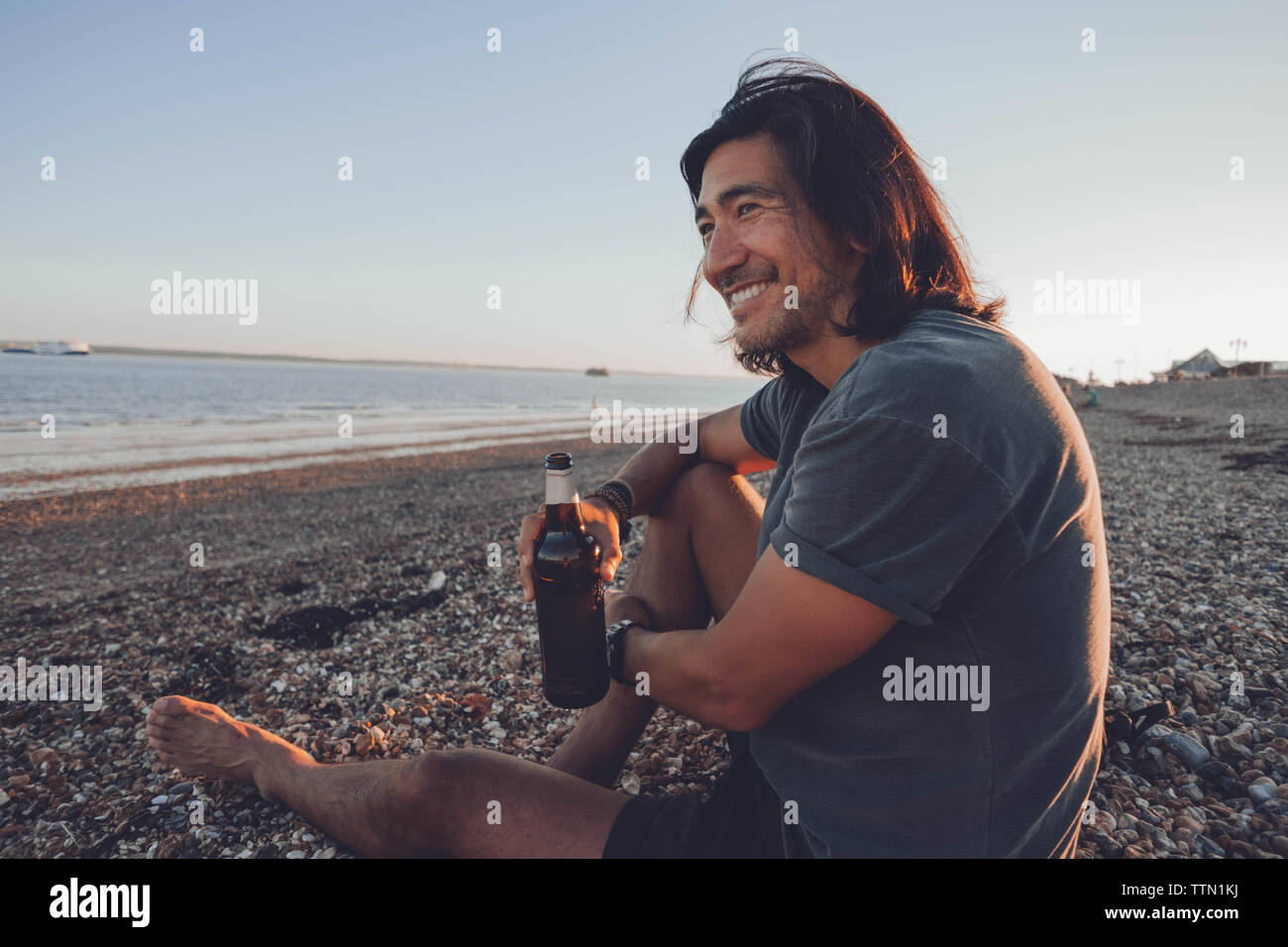 Person smiling at the camera on the beach while drinking a beer Stock Photo