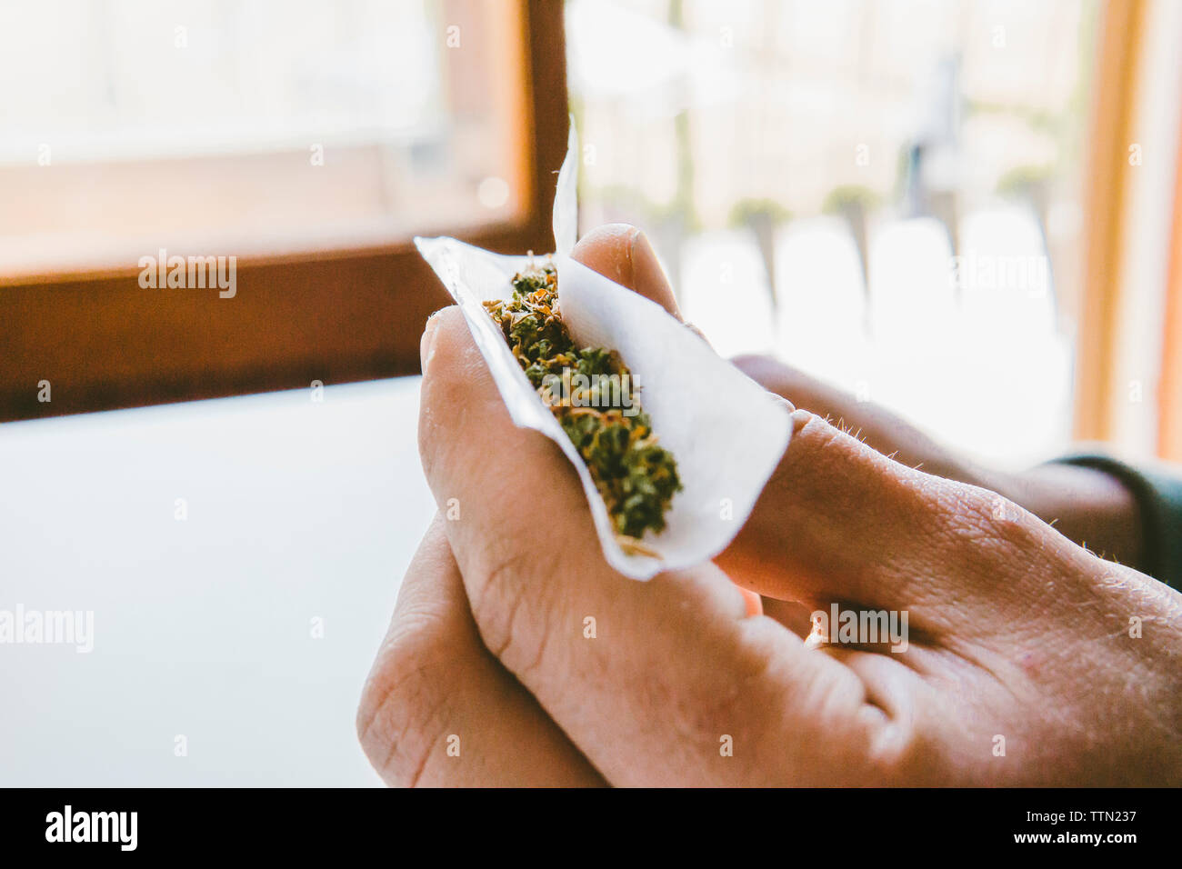 Cropped hand of man rolling marijuana joints in paper at home Stock Photo