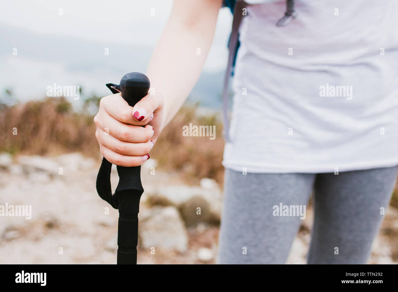 Midsection of female hiker holding hiking pole while standing on mountain Stock Photo