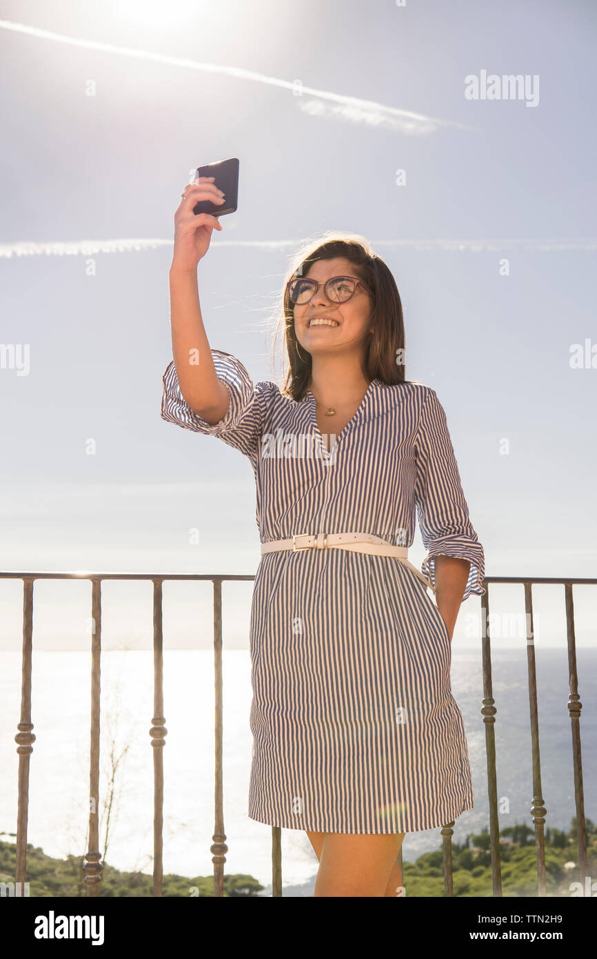 Smiling teenage girl taking selfie while standing by railing at observation point against sea Stock Photo