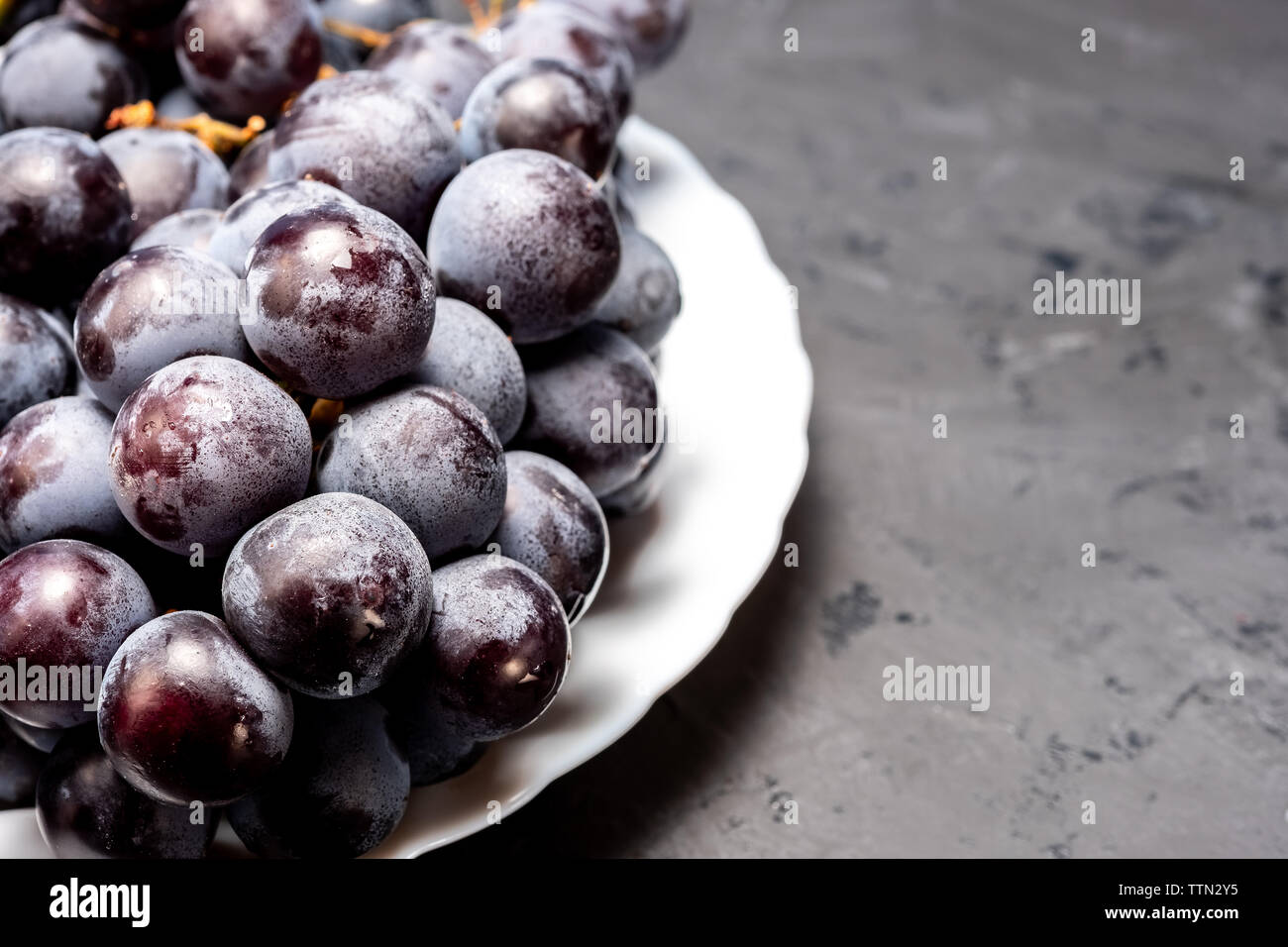 bunch of black ripe grapes on a white plate Stock Photo