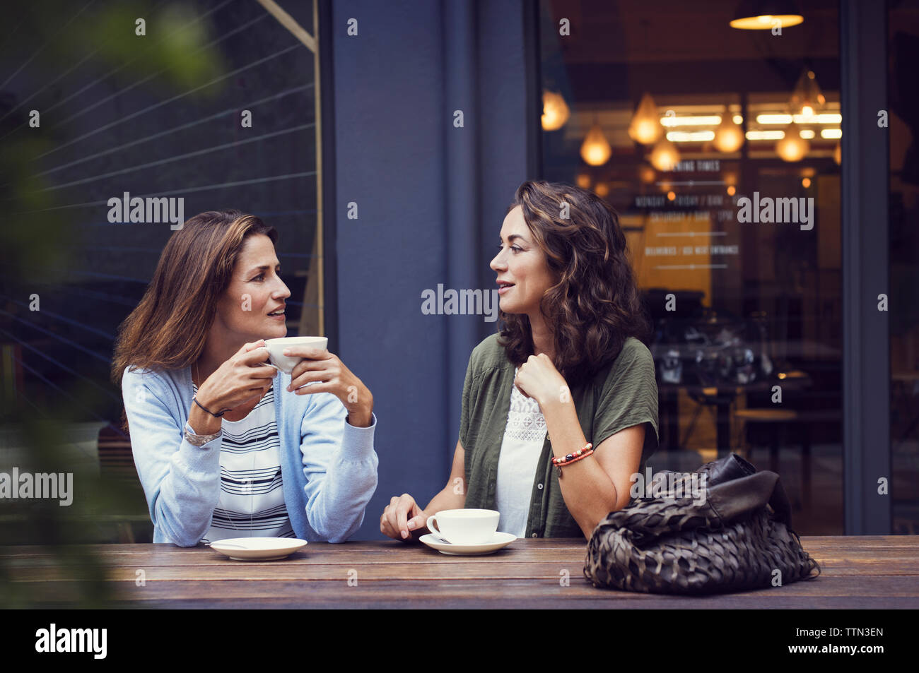 Female friends talking while having coffee at sidewalk cafe Stock Photo