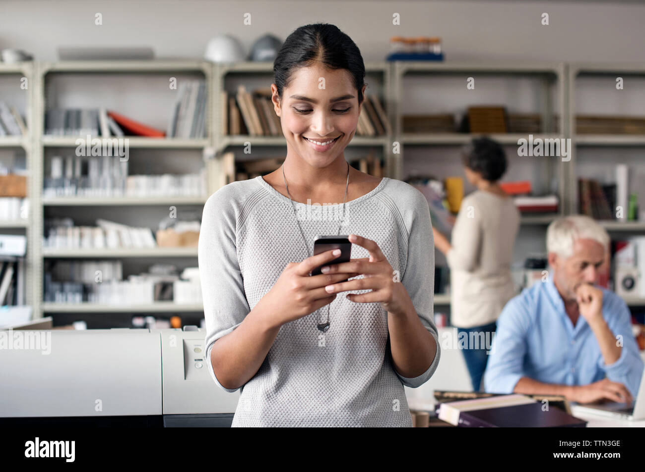Happy interior designer using smart phone with colleagues working in background Stock Photo