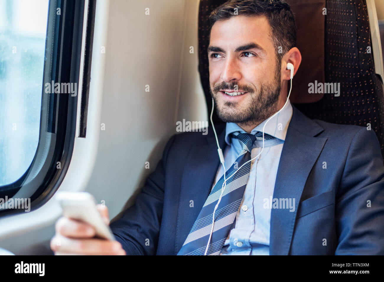 Smiling businessman listening music through smart phone in train Stock Photo