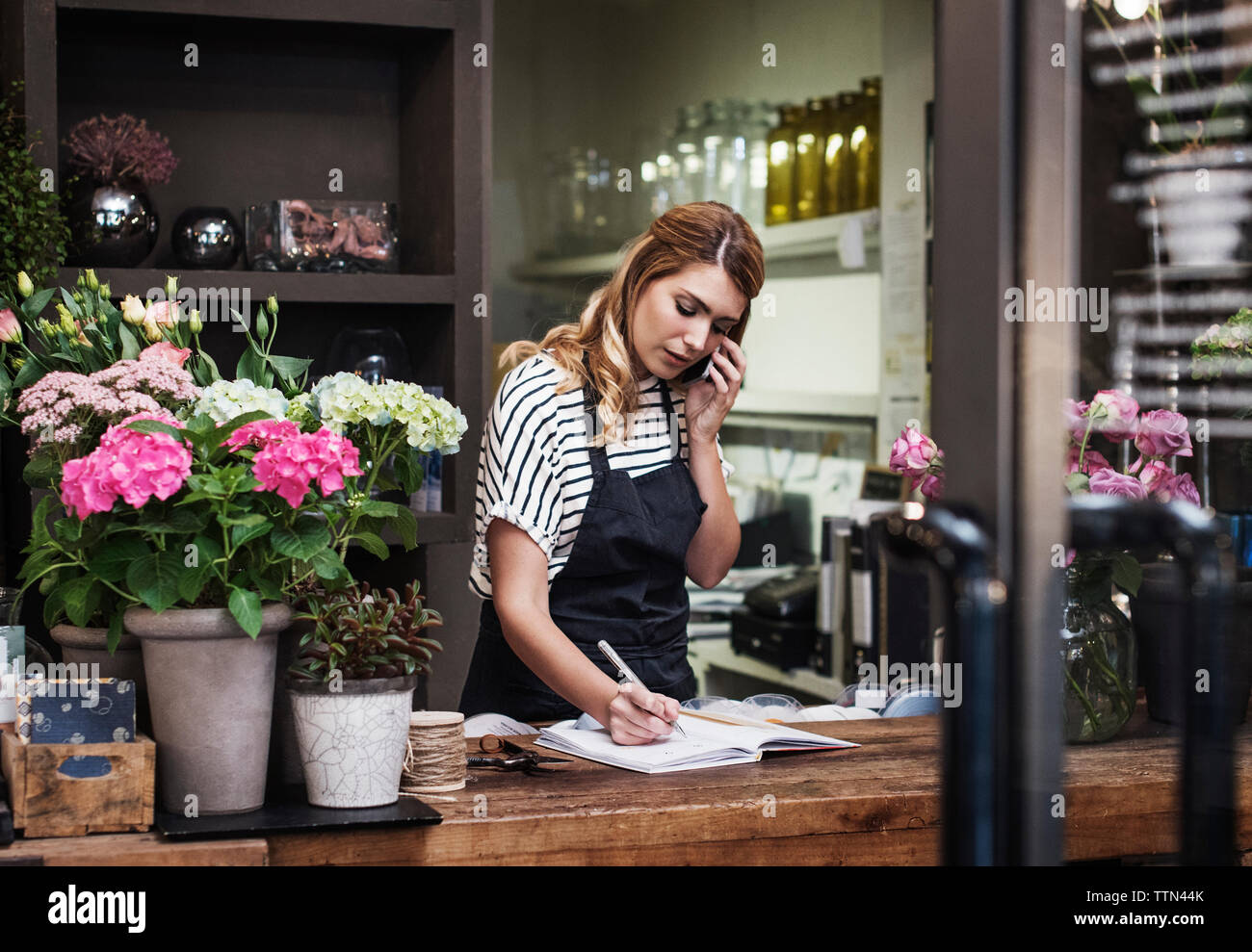 Florist writing in note pad while talking on mobile phone Stock Photo