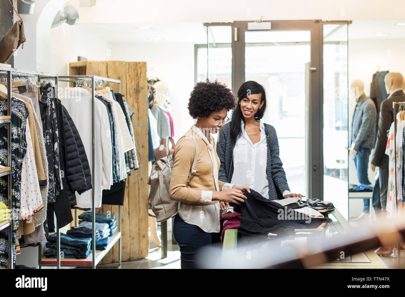 Friends talking while checking shirts at store on sunny day Stock Photo