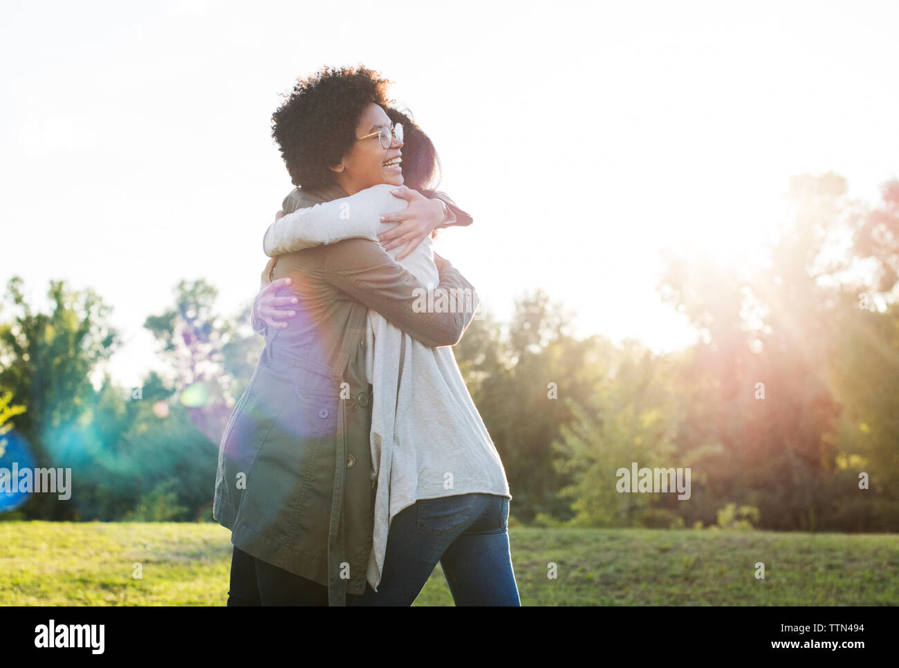 Smiling friends embracing on grassy field against clear sky Stock Photo