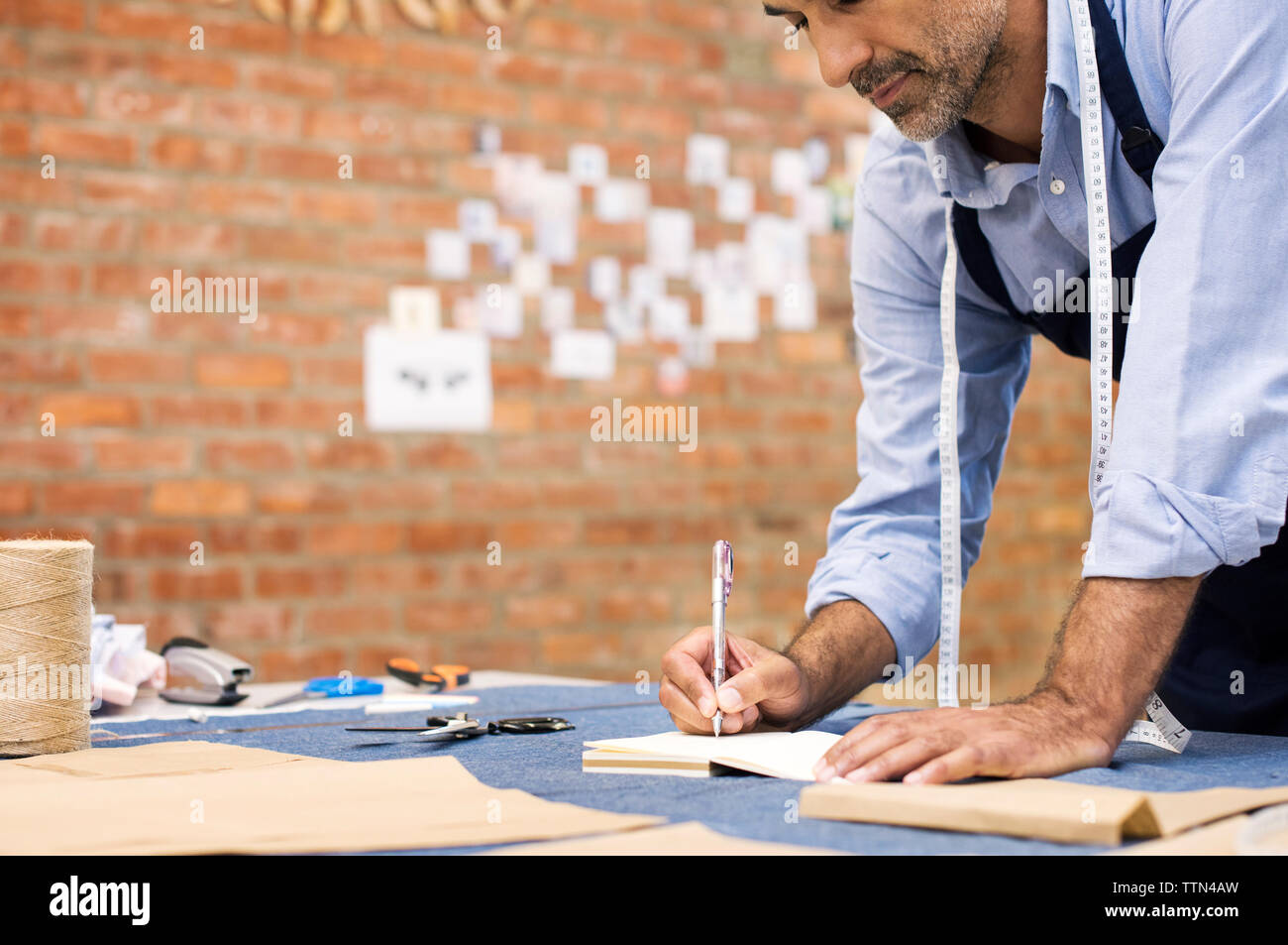 Male fashion designer writing while working at table in workshop Stock Photo
